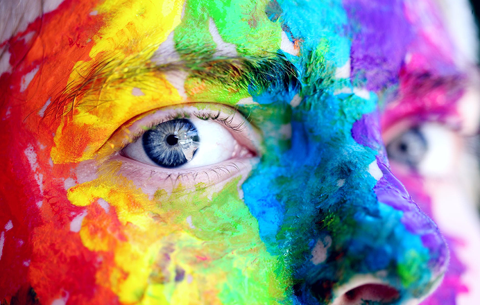 Close-up portrait of a face covered in vivid rainbow paint